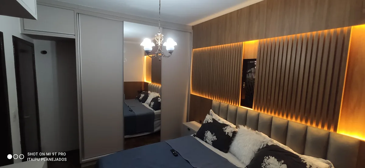 Quarto com cabeceira ripada em madeira e iluminação indireta